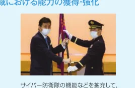 サイバー防衛隊の機能拡充に関連する、旗の授与式を行う二人の男性の写真