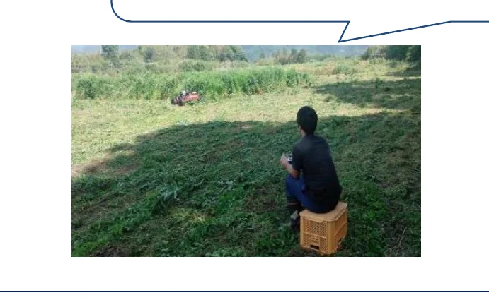 男性がリモコンを持って座り、遠くの芝刈り機を操作している。